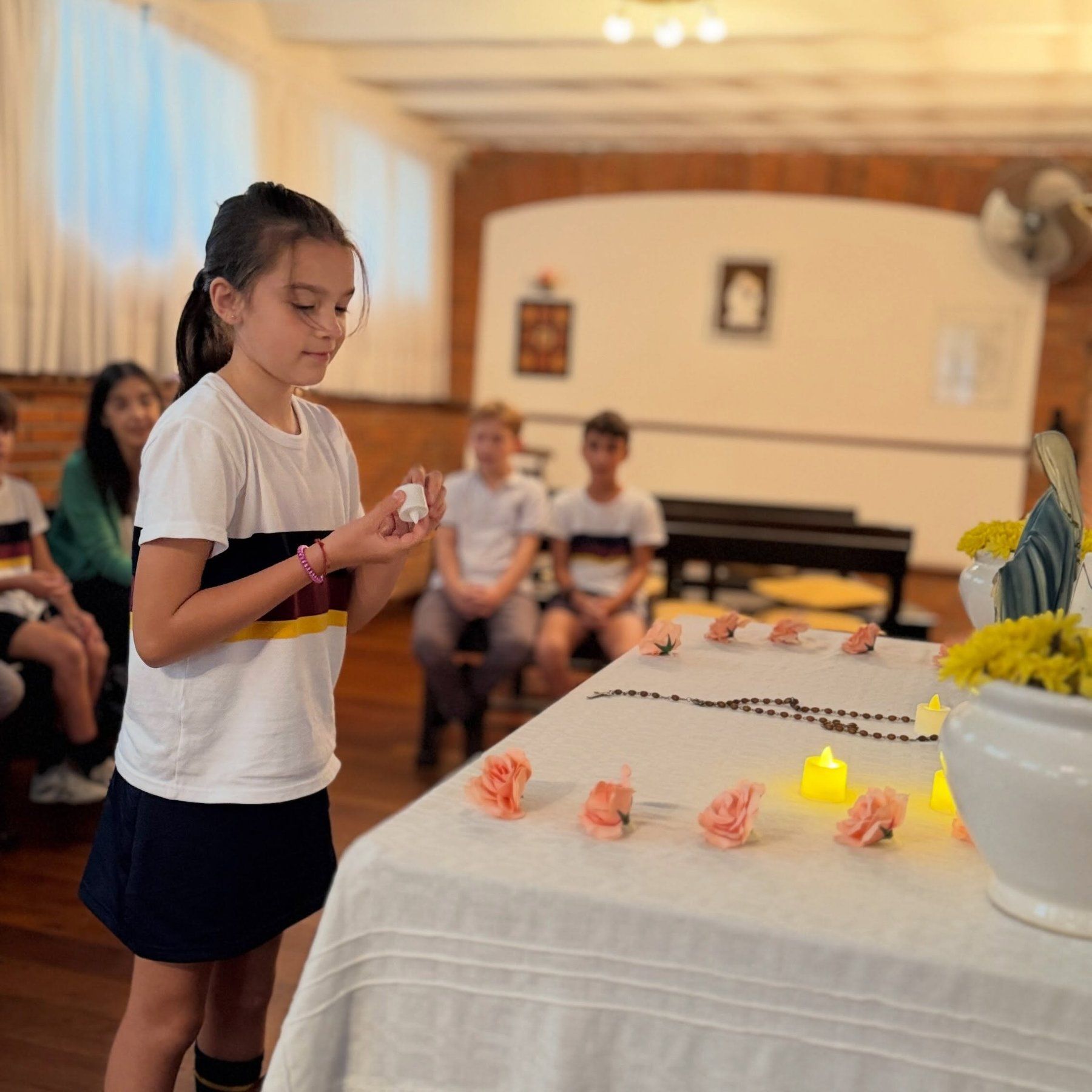 Una alumna deja una flor sobre la mesa del altar, entre velas encendidas