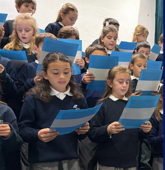 Alumnos de cuarto grado cantando con banderas argentinas en la Promesa a la Bandera